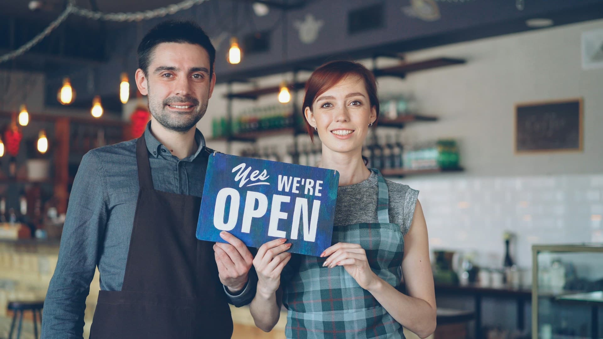 Two small business owners holding an open sign in their shop