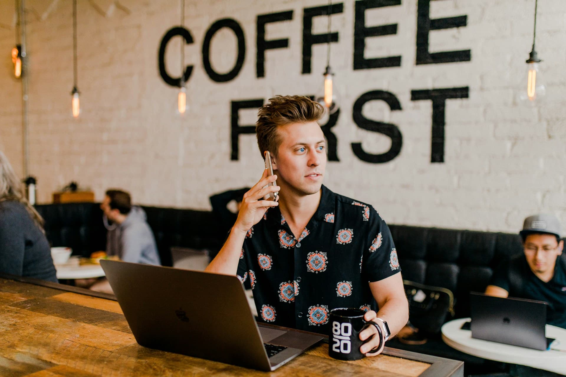 A young startup founder taking a business call in a coffee shop with a laptop